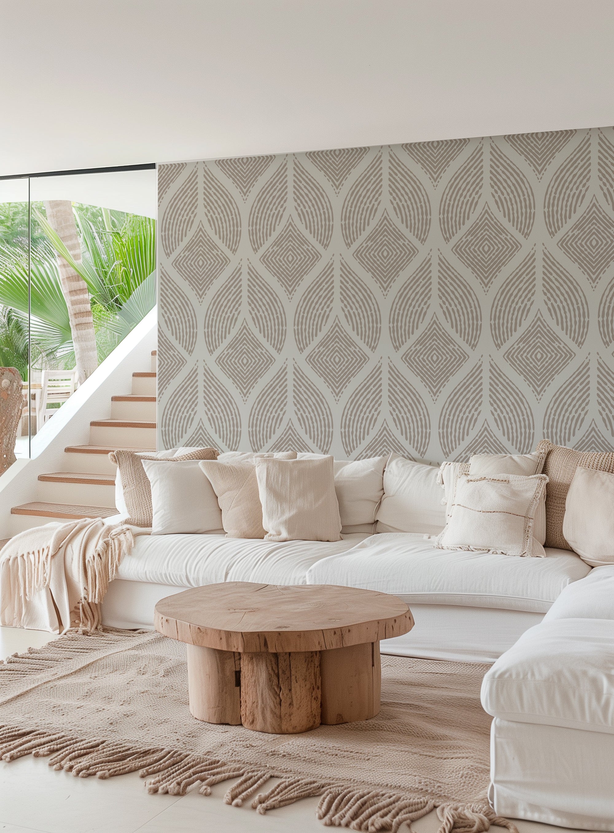 A modern living room featuring a large white sectional sofa with cream pillows, a round natural wood coffee table, and a prominent patterned wallpaper wall in warm beige and gray tones.